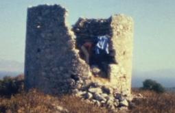 A person climbs inside an old rock fort, a blue shirt hangs on the edge.