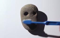 A rock with two cut outs resembling eyes is brushed with a toothbrush.