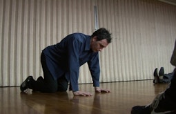 A person rests on the ground on their hands and knees during a performance.
