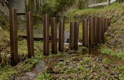 Metal stakes make a fence through a small stream.