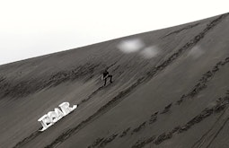 A person drags a white sculpture of the word FEAR up a large sand dune.