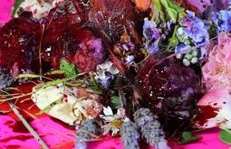 A collection of flowers and meat-like fluid and textures on a pink table.