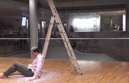 A man sits at the bottom of a ladder being covered in paper dust as a part of a performance.