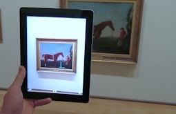A person looks at an old painting of a horse through an iPad's camera.