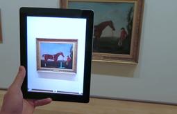 A person looks at an old painting of a horse through an iPad's camera.