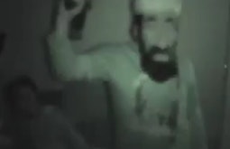 Seen through a night-vision camera a person wears a caricature mask of Osama Bin Laden.