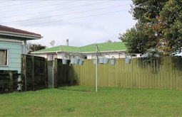In a backyard numerous buckets are pegged to a washing line. A tall fence stands behind the washing line.