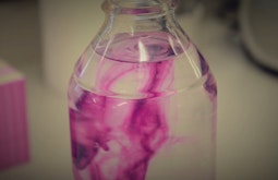 A water bottle with pink dye swirling in its contents.