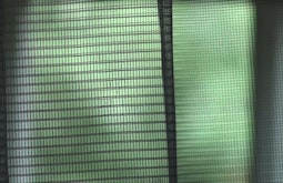An extreme close up of a mesh screen with green foliage obscured in the background.