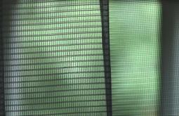 An extreme close up of a mesh screen with green foliage obscured in the background.