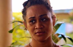 A close up of a woman looking out of frame. Leaves from plant appear behind her.