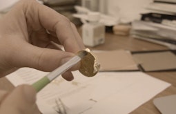 A hand carefully brushes gold leaf onto a handmade coin.
