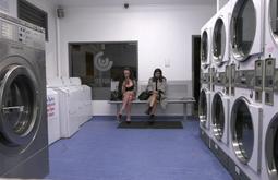 Two people sit cross legged in an otherwise empty laundromat.