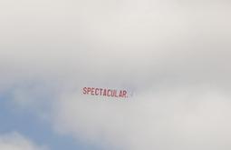 A large banner reading Spectacular flies behind a plane on a cloudy day.