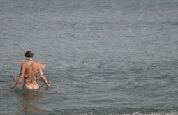 A person wades into the sea naked, their body becoming increasingly pixelated and distorted.