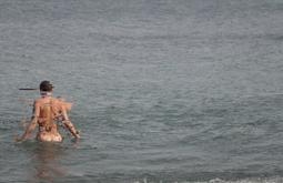 A person wades into the sea naked, their body becoming increasingly pixelated and distorted.