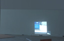 A film of a street is projected on a white wall.