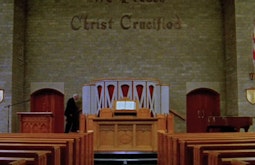 A person walks past the alter of a church, there are empty rows of pews in front. The Union Jack hangs off a back wall.