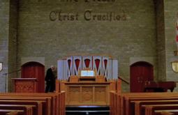 A person walks past the alter of a church, there are empty rows of pews in front. The Union Jack hangs off a back wall.