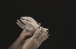 Two human hands hold a life-size figurine of hands that wear jewellery.