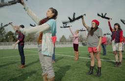 A group of people stand in lines on a field practicing manoeuvres with rifles.