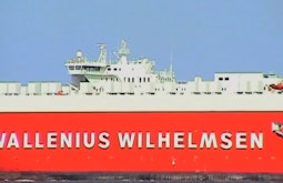 A bright red transport ship sails past, the name Wallenius Wilhelmsen is written on the side of the ship.