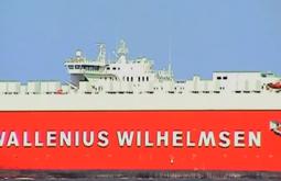 A bright red transport ship sails past, the name Wallenius Wilhelmsen is written on the side of the ship.