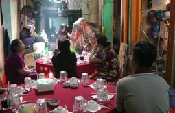 In an alley restaurant people sit having a meal. A man sits at a table set with bowls and glasses by himself.