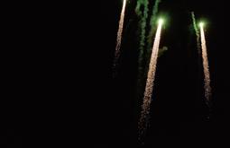 Three fireworks with spark trails shoot upwards on a dark night.