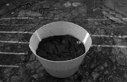 A white bucket with a sheet soaking in dye.