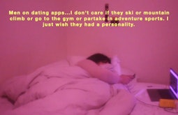 A  person lies in bed with an open laptop beside them while they're on their phone. The room is in pink light.