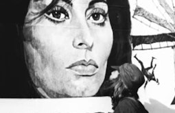 The artist kisses a billboard of Sophia Loren.