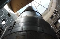 A large shiny metal rocket in a construction bay with a glass ceiling.