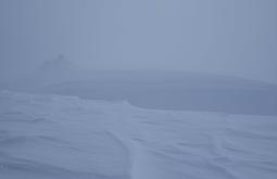 A landscape of snow, there is a hill in the distance through the fog.