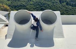 A person climes on a roof between to circular skylights.