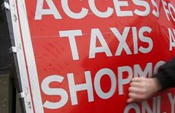 A fist hits a bight red sign that has the text "Access for taxis and shop..." some of the text is obscured.