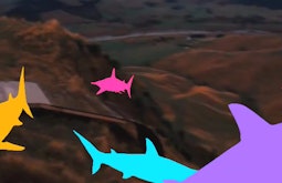 Multicoloured animated sharks swim above country hills.