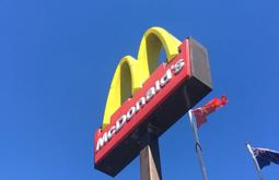 A McDonald's sign as seen from below, with deep blue sky above. The New Zealand flag flies beside it.