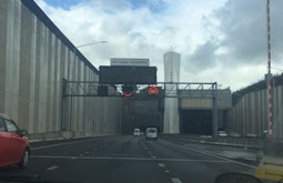 The view from the front seat of a car as it drives towards a large urban tunnel.