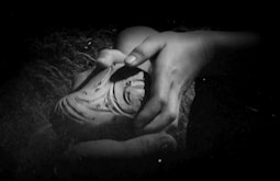 Two shadowy hands hold a Māori carving.