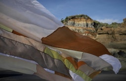 A thin patchwork cloth blows in the wind on the beach. Tall cliffs stand in the distance.