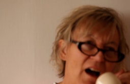 An out of focus woman wearing black glasses talks into a phone.