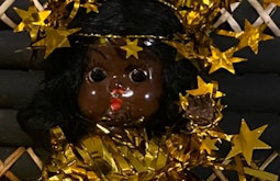 A brown children's doll is shrouded in gold stars and tinsel.