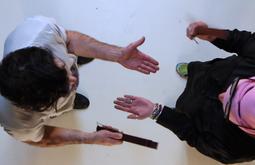 A birds-eye view of two people as they stand using straps to slap each-others open palms.