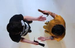 A birds-eye view of two people as they stand using straps to slap each-others open palms.