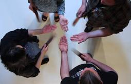 A birds-eye view of four people as they stand using straps to slap each-others open palms.