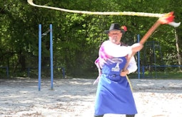 A person stands in a sandy park cracking a large whip.
