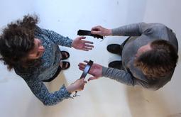 A birds-eye view of two people as they stand using straps to slap each-others open palms.