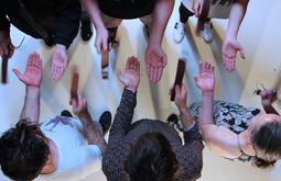 A birds-eye view of six people as they stand using straps to slap each-others open palms.