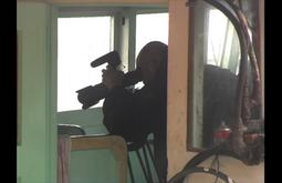 A person holds a camera out a window, they're looking through the viewfinder.